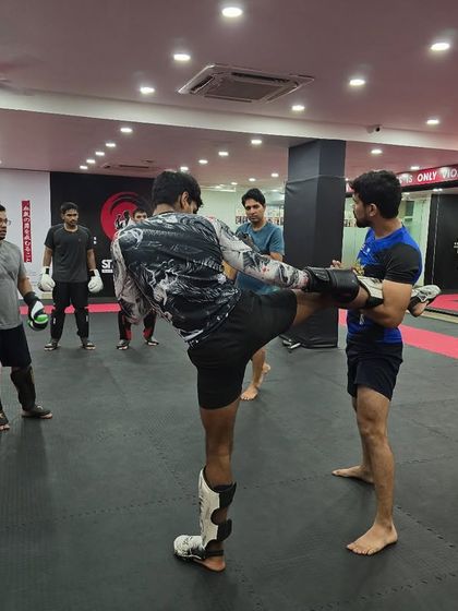 In our beginner classes, we break down the fundamentals. A coach holds pads for a student, ensuring they develop the correct form and power for a foundational kickboxing roundhouse kick.