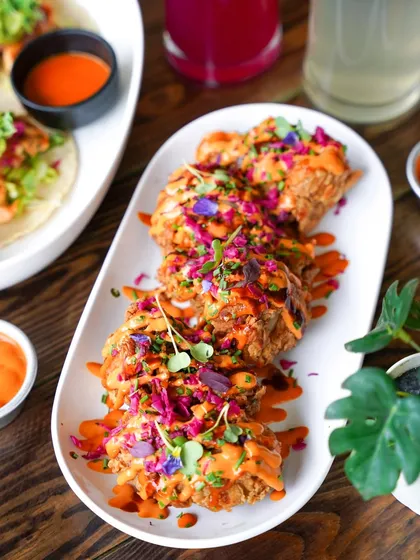 A platter of crispy fried chicken topped with colorful sauces and microgreens. The bright, clean photography makes this appetizer look incredibly crunchy and flavorful.
