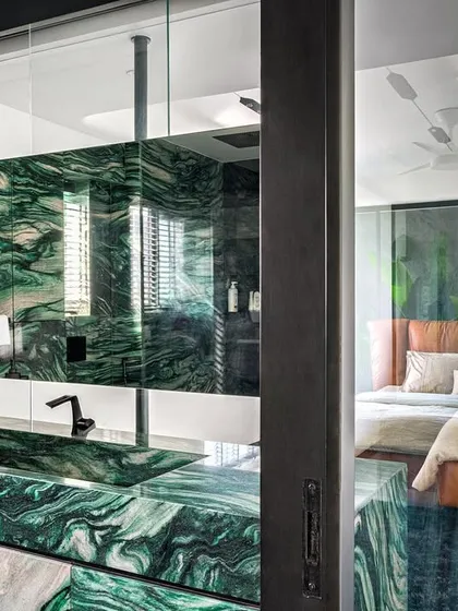We often use bold materials to create dramatic focal points. In this master suite, a wall of jade green marble seamlessly integrates the vanity and basin, flowing from the bath space into the bedroom and creating a powerful visual connection between the two zones.