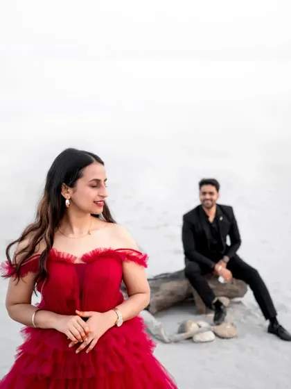 A striking contrast. Ishu's vibrant red gown stands out against the stark, white sands, while Arihant looks on with a smile. This image shows how I play with color and composition to create visually compelling portraits.
