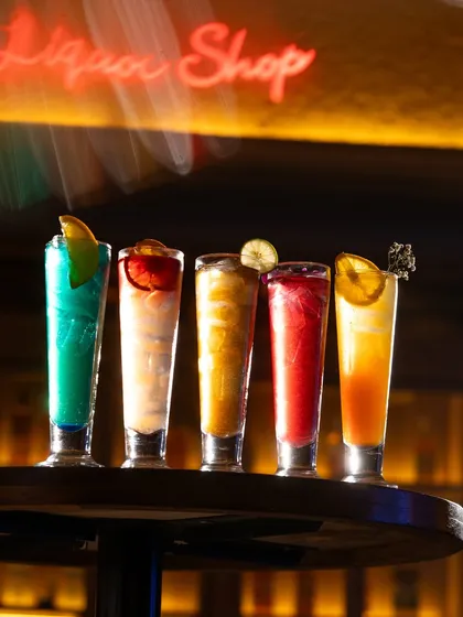 A vibrant lineup of colorful cocktails against a moody bar backdrop. This type of shot is perfect for showcasing the range and visual appeal of a new beverage menu.