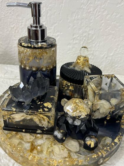 A complete bathroom organizer set made with real rose petals, pearls, and gold flakes. The set includes a tray, soap dispenser, jar, holder, and a cute teddy bear figure, all in a luxurious black and gold theme.