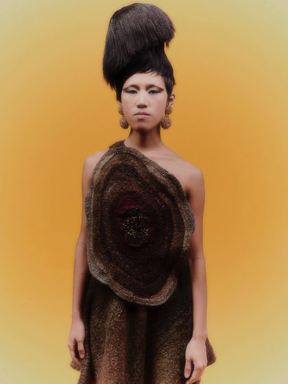 A full-length view of the avant-garde look, showing how the statement earrings balance the sculptural quality of the dress and the dramatic hair.