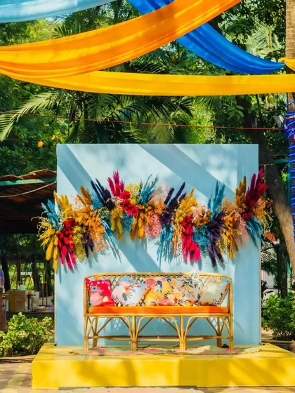 A vibrant and quirky photo booth, featuring a comfortable bench set against a bright blue wall with a stunning arrangement of multi-colored dried flowers.