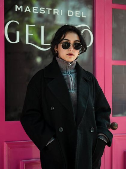 This street style shot combines fashion with a vibrant urban background. The model's chic winter coat and sunglasses are contrasted against a bright pink door, creating a memorable and eye-catching image.