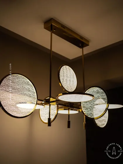 Modern artistry meets functional lighting in this unique chandelier. Featuring textured, disc-shaped diffusers on a brass frame, it provides warm, even light, making it a perfect statement piece over a contemporary dining table.