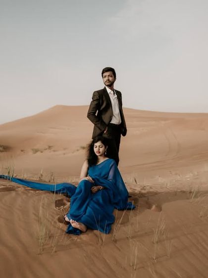 A dramatic pose in the vast Dubai desert, with the groom standing and the bride seated, creating a powerful and artistic composition.