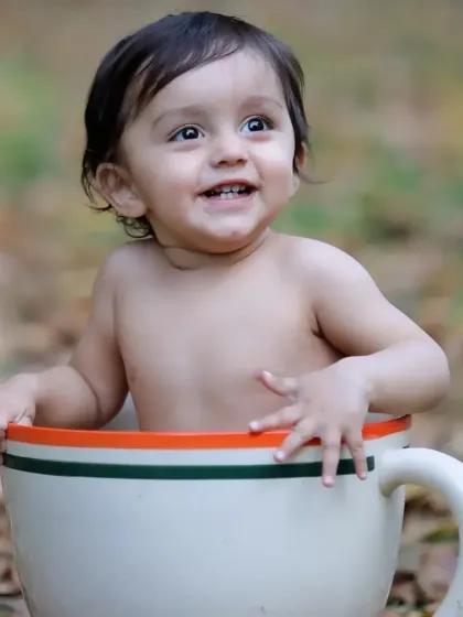 A happy baby boy with a big smile, posing in our giant teacup prop during an outdoor session among autumn leaves.