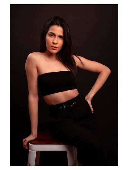 A minimalist fashion portrait against a dark background. The simple tube top and trousers create a clean, modern silhouette.