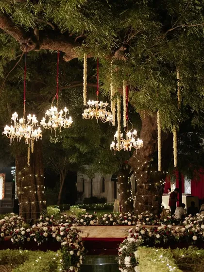 Enchanting decor where chandeliers and floral strings are hung from the branches of old trees, blending natural beauty with glamorous design.