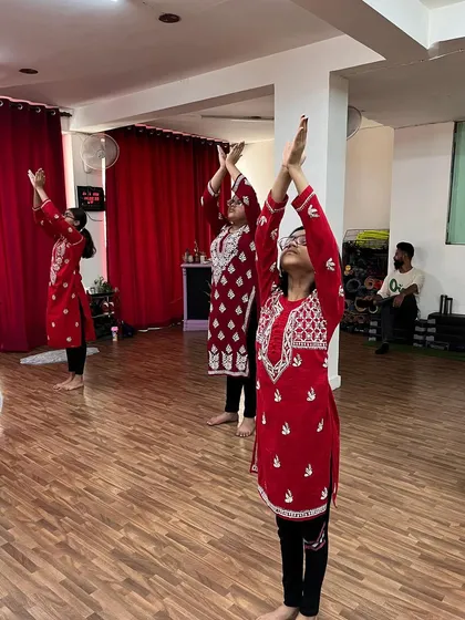 A group of students in matching red kurtas, fully absorbed in their semi classical practice. Their upward gaze shows their deep connection to the movement.