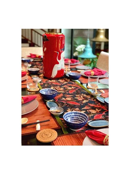 A vibrant, Asian-themed tablescape with a red crane vase, patterned runner, and blue and white ceramic bowls.
