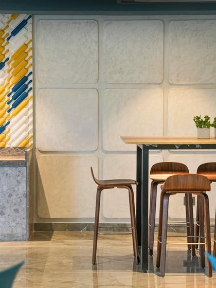 A detail from the Trilogy clubhouse, showing a high-top seating area. The design incorporates tactile materials like the yellow and blue acoustic wall panel, adding both visual interest and functional sound absorption to the space.