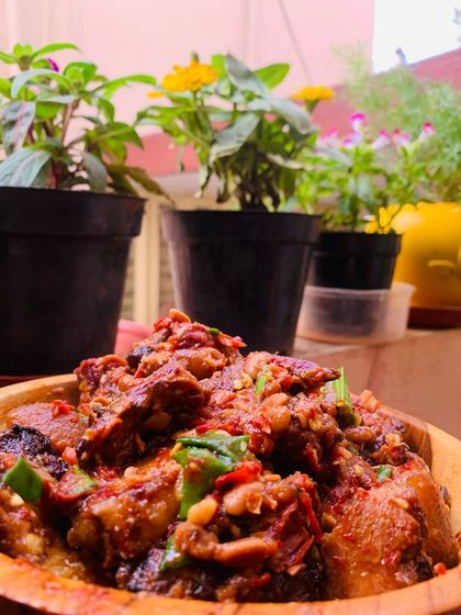 A bowl of delicious smoked pork cooked with axone, dried red chillies, and tomatoes, garnished with fresh spring onion.