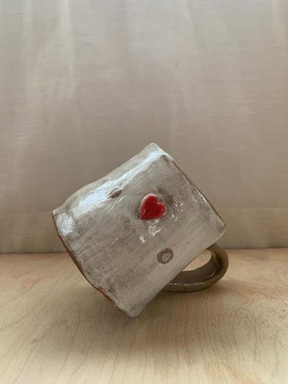 A rustic, heart-adorned mug made by a student, tilted to show its unique character. This piece tells a story of learning, patience, and the love of making.