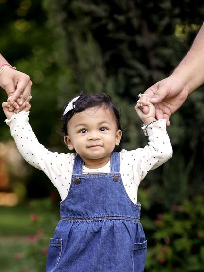 A toddler holds her parents' hands and looks up at the camera, a perfect shot capturing a key milestone.