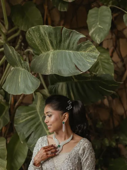 A fresh and vibrant bridal portrait. The lush green leaves in the background provide a beautiful natural frame, highlighting the bride's radiant smile.