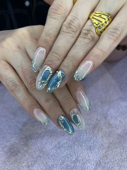 An elegant and intricate design with a soft ombre base, silver glitter tips, and blue stone-like 3D accents.