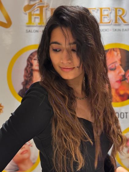 A client showing off her long, wavy hair with a fresh color. The look is natural and beautiful, with a healthy shine that makes her glow.