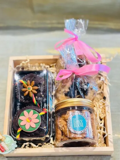 This Rakhi gift hamper includes Rakhi-themed chocolate cupcakes, a jar of our signature cookies, and other assorted goodies, all packed in a rustic wooden tray.