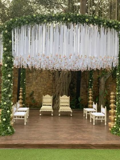 A round mandap design framed with lush greenery and white ribbon details. The use of traditional golden pillars adds a classic touch to this modern and elegant structure.