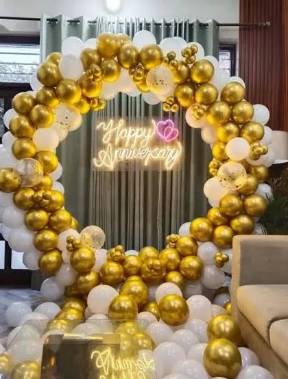 A luxurious anniversary setup in a living room, featuring a full circular balloon arch in gold and white with a neon sign.