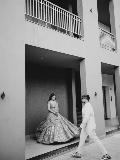 A creative black and white portrait. The composition, with the groom walking towards his bride, creates a sense of anticipation and story.