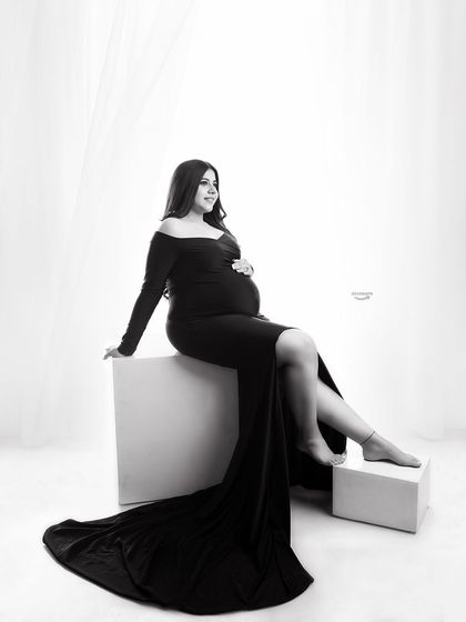 A classic black and white studio portrait. The client is seated in an elegant black gown against a bright, clean background, creating a timeless and sophisticated look.