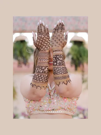 A playful shot of the bride peeking through her henna-covered hands. This classic Mehendi pose is captured with a focus on the intricate design.