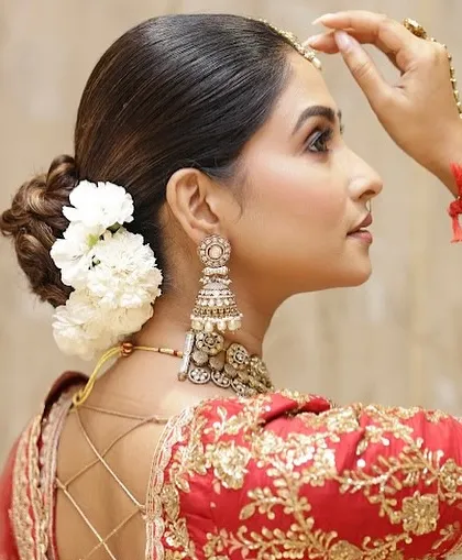 A detailed profile shot showing the harmony between the makeup, the intricate low bun hairstyle with fresh flowers, and the elegant blouse design. I teach my students to have an eye for these complete details.