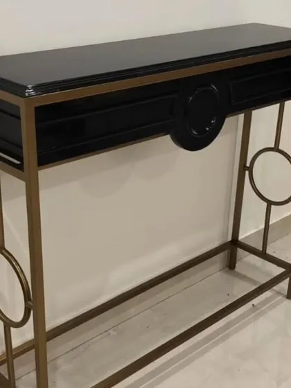 A console table that combines a black lacquered top with a sculptural gold-finished frame. The circular motifs on the legs add a geometric, artistic element to this functional and elegant piece.