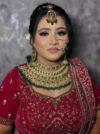 A classic bridal portrait. This bride's makeup features a soft smokey eye and a matte nude lip, perfectly balancing her heavy red velvet lehenga and gold jewelry.