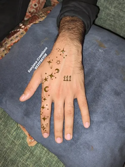 A close-up of a modern henna design for men, featuring a scatter of stars, crescent moons, and the number '111'. It's a stylish and personal statement.