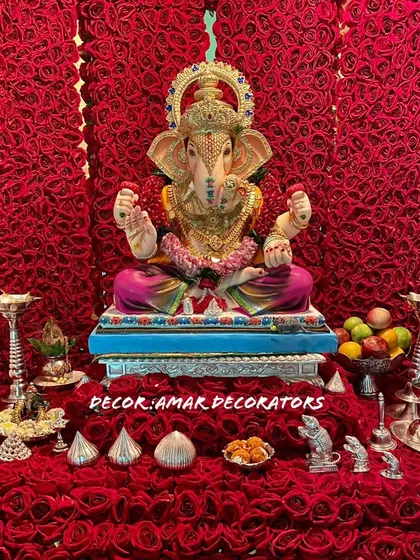 A close up of the Ganpati idol against the rich red rose backdrop. The silver puja accessories and modaks stand out beautifully against the vibrant color.