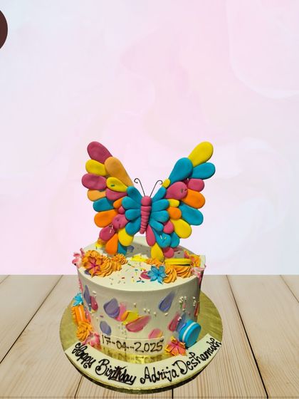 A vibrant and colorful butterfly cake perfect for a cheerful celebration. The topper is a large, multi-colored butterfly, and the cake is decorated with smaller edible butterflies and macarons.