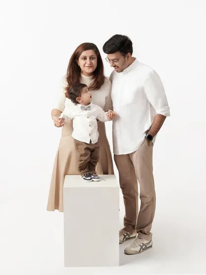 A candid family portrait where the parents are looking lovingly at their son, who is standing on a white block between them.