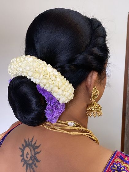 A classic low bun adorned with a jasmine gajra and a touch of purple flowers to match the client's saree.