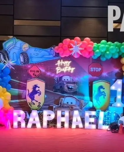 A high-energy Disney Cars theme for Raphael's first birthday. The setup includes character cutouts of Lightning McQueen and Mater, a racetrack-inspired backdrop, and marquee letters spelling out the name.