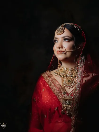 A classic, painterly portrait of the bride against a dark background, her golden jewelry and red outfit glowing in the soft light.