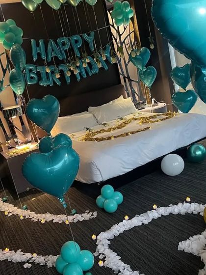 This setup features a pathway of white petals leading to the bed, with teal heart-shaped balloons floating throughout the room.