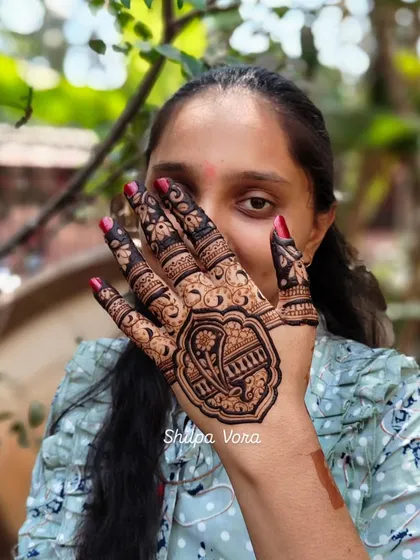 A client playfully hiding behind her hand, which is adorned with a large, intricate paisley design.