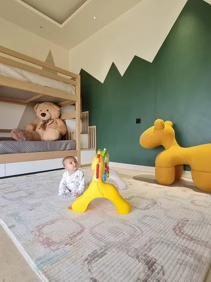 A ground-level view of the kids' bedroom, showing the fun and functional design. The space includes a soft play mat, whimsical animal-shaped furniture, and a custom green and grey mountain mural that sparks imagination.