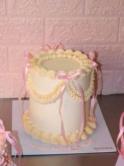 A full view of our white vintage cake adorned with pink ribbons. The intricate piping work and classic design make it a timeless choice for any special occasion.