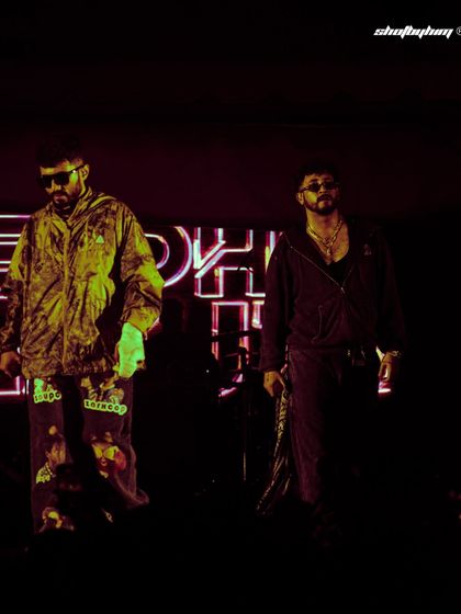 The duo Seedhe Maut walking on stage with neon signs glowing behind them. This shot captures the cool, confident entrance of the artists.