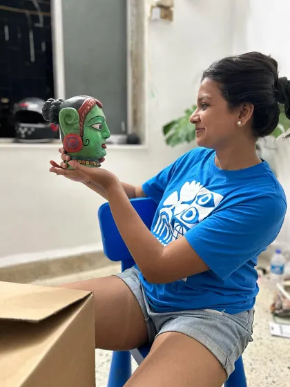 A playful moment in the studio, holding up a small, sculpted head. The creative process is not always serious; it's also about experimentation and fun.