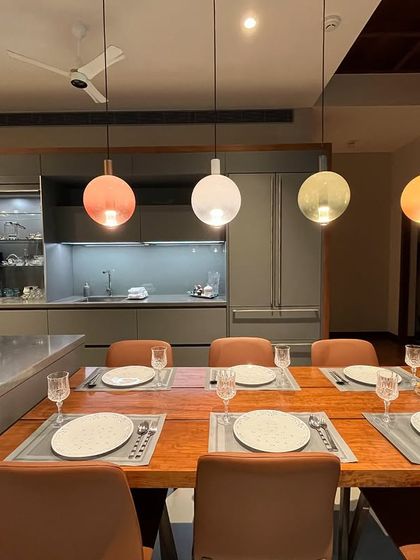 The dining table is integrated into the kitchen space in the Paul residence, creating a seamless area for cooking, dining, and socializing. The colorful pendant lights add a playful touch.