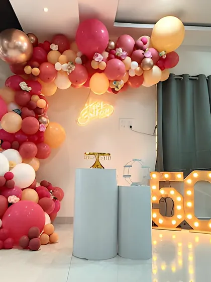 A beautiful 50th birthday decoration for a home party. The setup includes an organic balloon arch in shades of pink and peach, with large marquee numbers and cake stands.