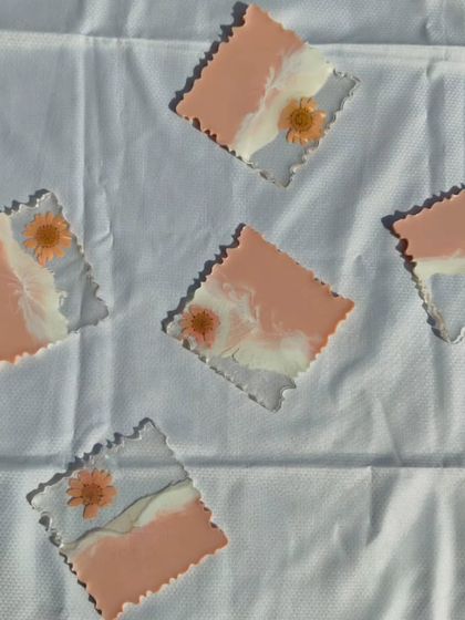 A set of five square resin coasters with a unique design. They feature a peachy-pink and white wave pattern with a single dried flower embedded in the corner, offering a soft, minimalist aesthetic.