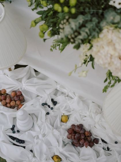 Textured and organic opulence. This pre-wedding dinner setup features layered drapes, wild florals, and scattered fruits for an effortlessly graceful look.