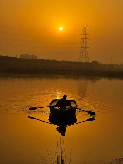A lone boatman rowing at sunset. The perfect reflection on the water and the golden light create a serene and beautifully symmetrical composition.